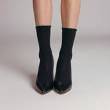 Black high-heeled shoes worn with black socks on a neutral background thumbnail