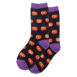 Child wearing glow-in-the-dark black socks with orange pumpkin patterns on a light wooden floor.