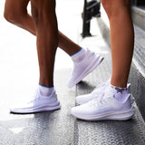 Two pairs of white sneakers worn by different people on a concrete surface.