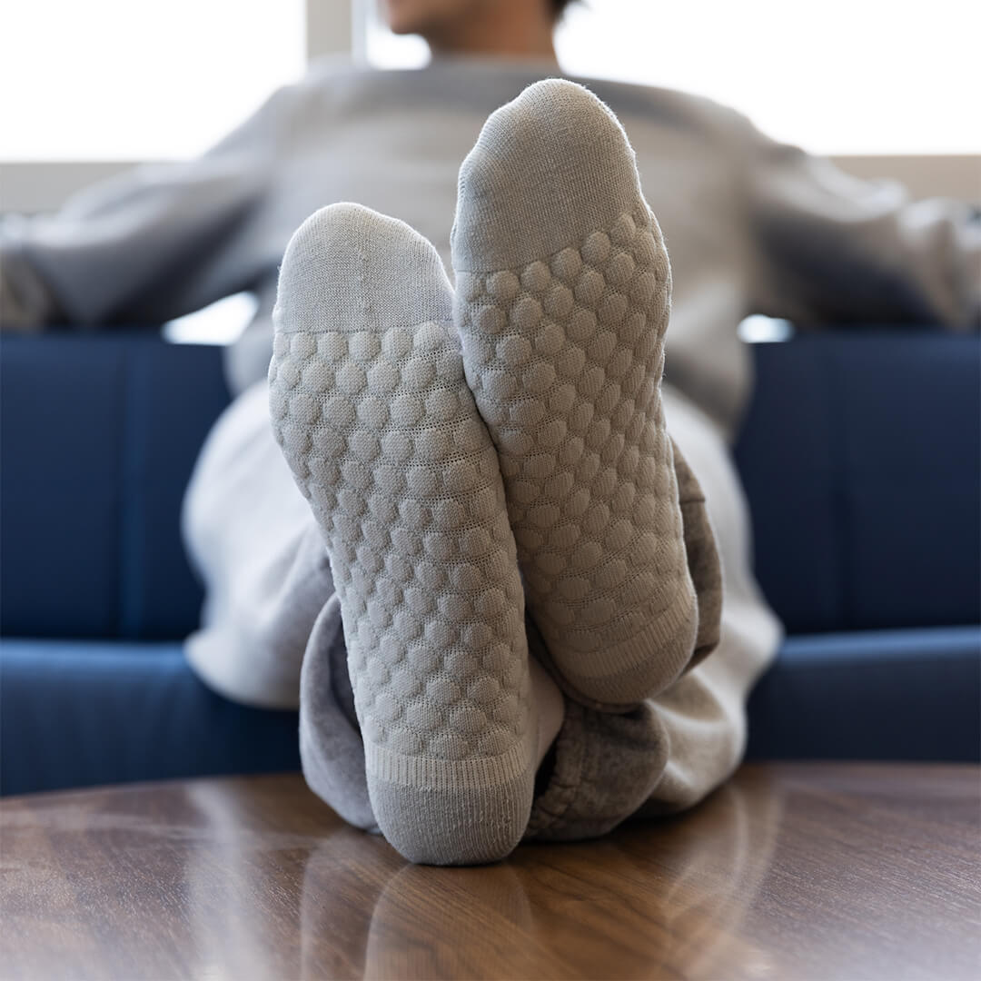 A person reclining on a blue couch with their feet up on a wooden table, wearing light gray textured socks with a raised bubble pattern on the soles.