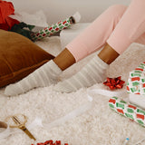 Person wearing fluffy socks on a carpeted floor with Christmas wrapping paper and ribbons. thumbnail
