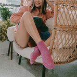 Person sitting on a wicker chair wearing colorful, fuzzy pink socks.