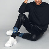 Person wearing black outfit with blue patterned socks sitting on a gray floor.