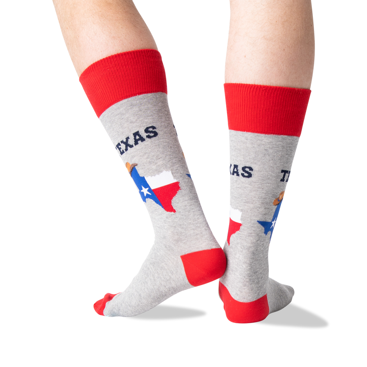 A person's legs wearing heather gray crew socks with red cuffs, heels, and toes, featuring a graphic of the state of Texas with the Texas flag and the word 'TEXAS'.