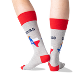 A person's legs wearing heather gray crew socks with red cuffs, heels, and toes, featuring a graphic of the state of Texas with the Texas flag and the word 'TEXAS'. thumbnail