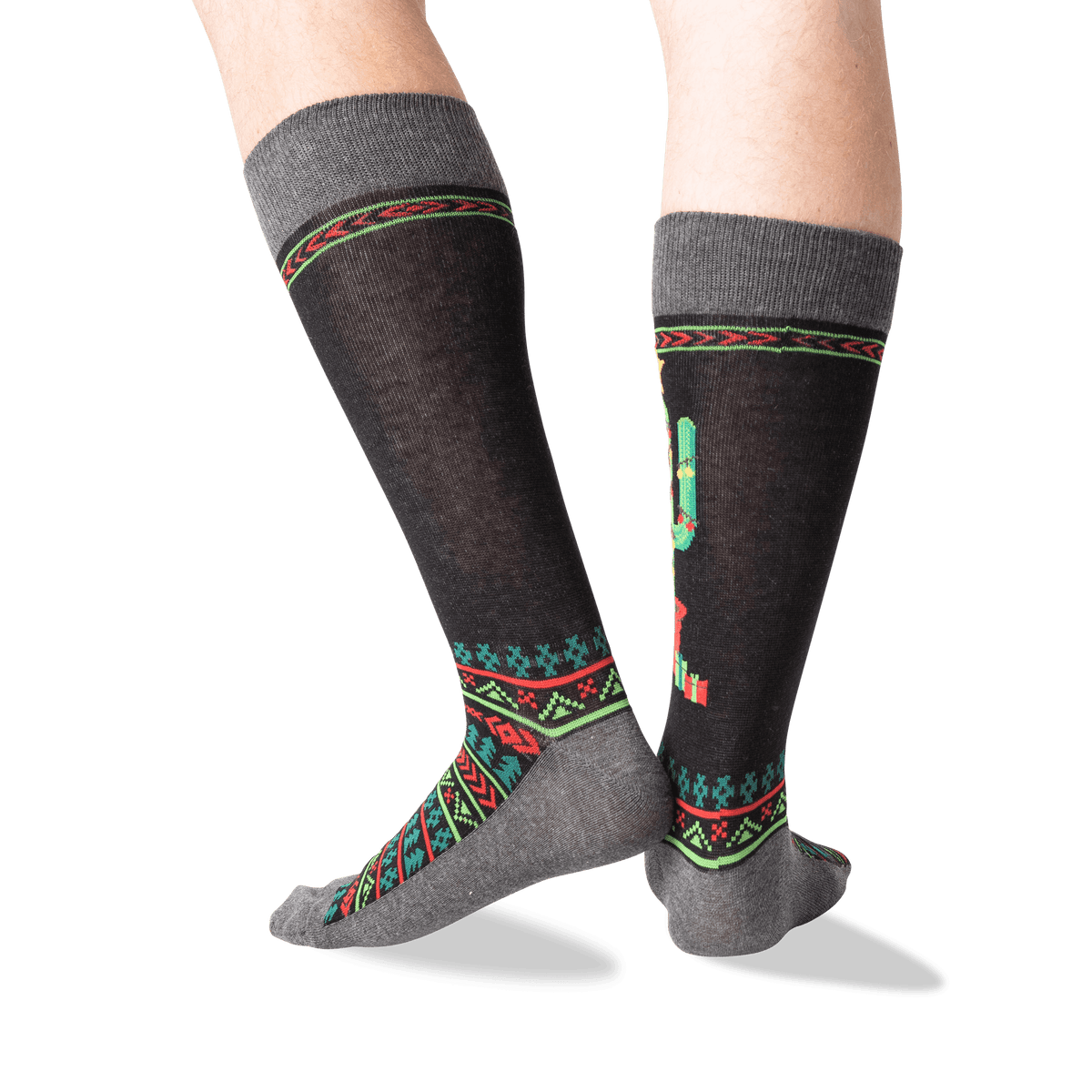 A pair of crew socks worn on a person's legs, featuring a dark charcoal gray base with a colorful geometric pattern in red, green, and teal, and a cactus motif on the side.