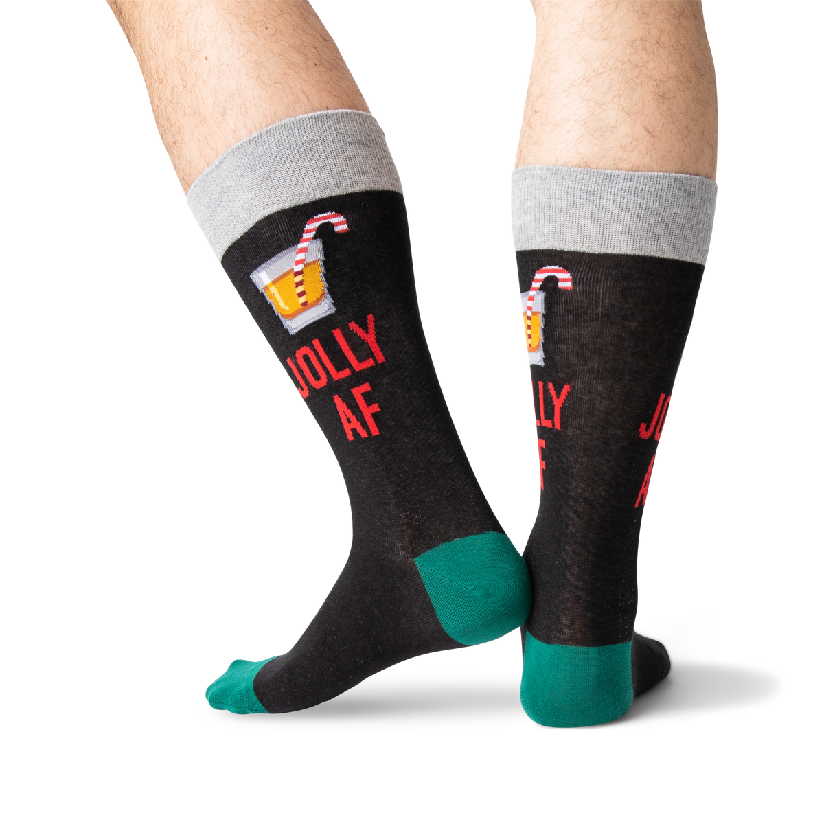 A pair of novelty crew socks worn on a person's legs, featuring a dark charcoal body with a gray cuff, green heels and toes, red text reading 'JOLLY AF', and a small cocktail graphic on the upper calf.