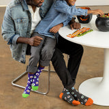 Two people sitting at a table with colorful socks on, one person is reaching into a cauldron. thumbnail