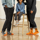 Child sitting on a stool with two adults wearing colorful socks in a casual setting. thumbnail