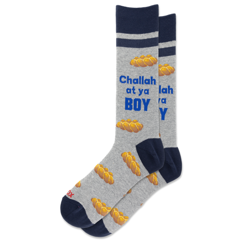A pair of crew socks in heather gray with navy blue cuffs, heels, and toes, featuring a pattern of golden matzah bread and the text 'Challah at ya BOY' in blue and white.