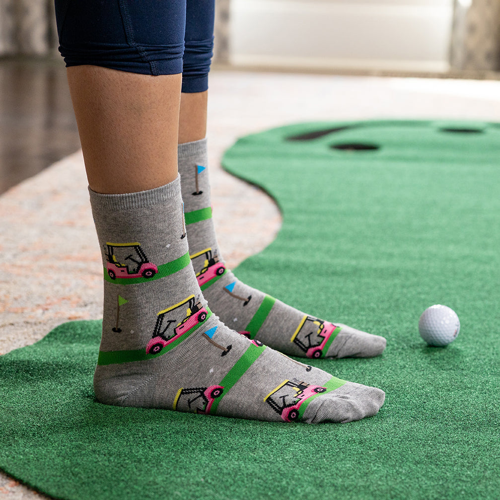 Person wearing gray socks with golf cart design on a putting green