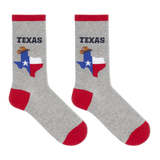A pair of heather gray crew socks with red cuffs, heels, and toes. Each sock features a graphic of the state of Texas filled with the Texas flag and a cowboy hat, with the word 'TEXAS' printed above in dark navy.