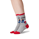 A pair of crew socks worn on a person's feet, shown against a plain white background. The socks are heather gray with red toes, heels, and cuffs, featuring a graphic of the state of Texas with a football player and the text 'TEXAS'.