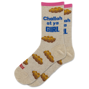 A pair of beige crew socks with a pink cuff, featuring a pattern of braided bread loops and blue text that reads 'Challah at ya GIRL'. One sock also has red text reading 'Sax' near the toe.