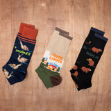 Three pairs of socks with humorous designs on a burlap background thumbnail