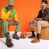Two men sitting on stools against an orange background wearing and camping-themed socks.