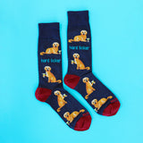 A pair of navy blue crew socks with a repeating pattern of a golden retriever dog holding a cocktail glass and the text 'hard licker', with red heels and toes, displayed on a bright cyan background.
