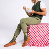 Man sitting on a red and white checkered tablecloth, wearing green socks with pasta print.