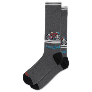 A pair of dark heather gray crew socks with black heels and toes, featuring a colorful bicycle graphic and the text 'two tired' in blue, on a plain white background.
