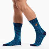 A pair of crew socks with horizontal blue and black stripes, worn on a model's legs against a clean white background. A small orange and yellow logo is visible on the side of the right sock.