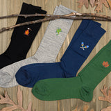 Four pairs of socks in black, gray, blue, and green with embroidered designs on a wooden surface.