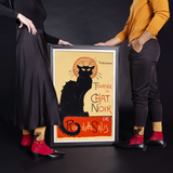 Two people holding a framed poster of a black cat with text, against a dark background. thumbnail