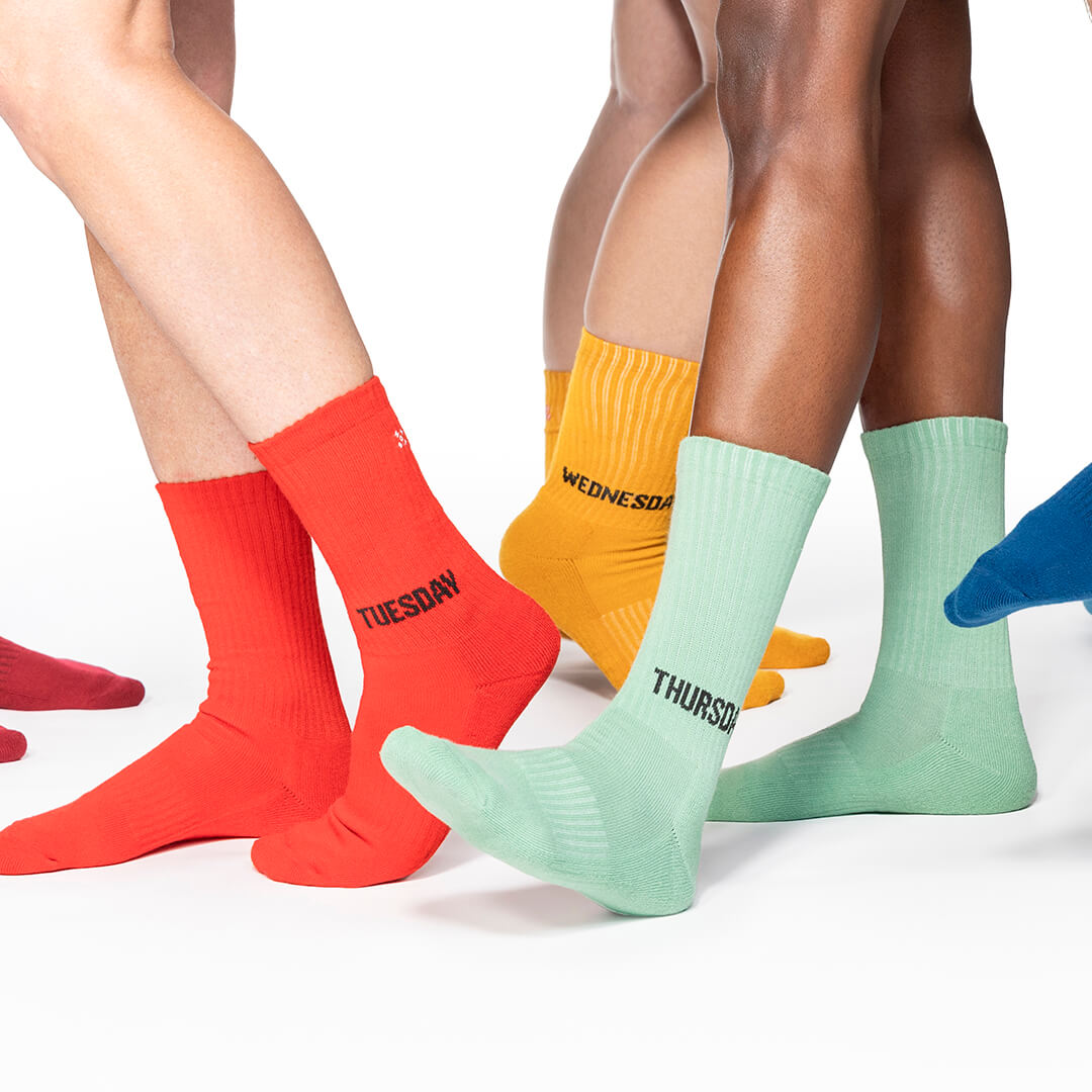 Colorful socks labeled for each day of the week worn by multiple people on a white background