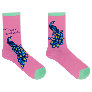 A pair of pink crew socks with mint green toes and heels, featuring a large blue and green peacock design and the text 'always sparkle' on one sock, shown on a white background.