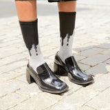 Black patent leather shoes worn with socks featuring a dripping design on a stone pavement. thumbnail