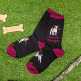 Black socks with dog illustrations and 'branch manager' text on a grass background with bones and sticks.