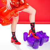 Person wearing red shoes and black socks with red and pink gummy bears, standing on a purple inflatable object against a red background.