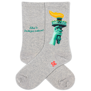 A pair of heather gray crew socks featuring a graphic of the Statue of Liberty's hand holding a yellow torch, with the text 'She's Independent' printed in teal on the other sock. A small red and white 'HOTSOX' logo is visible near the ankle.