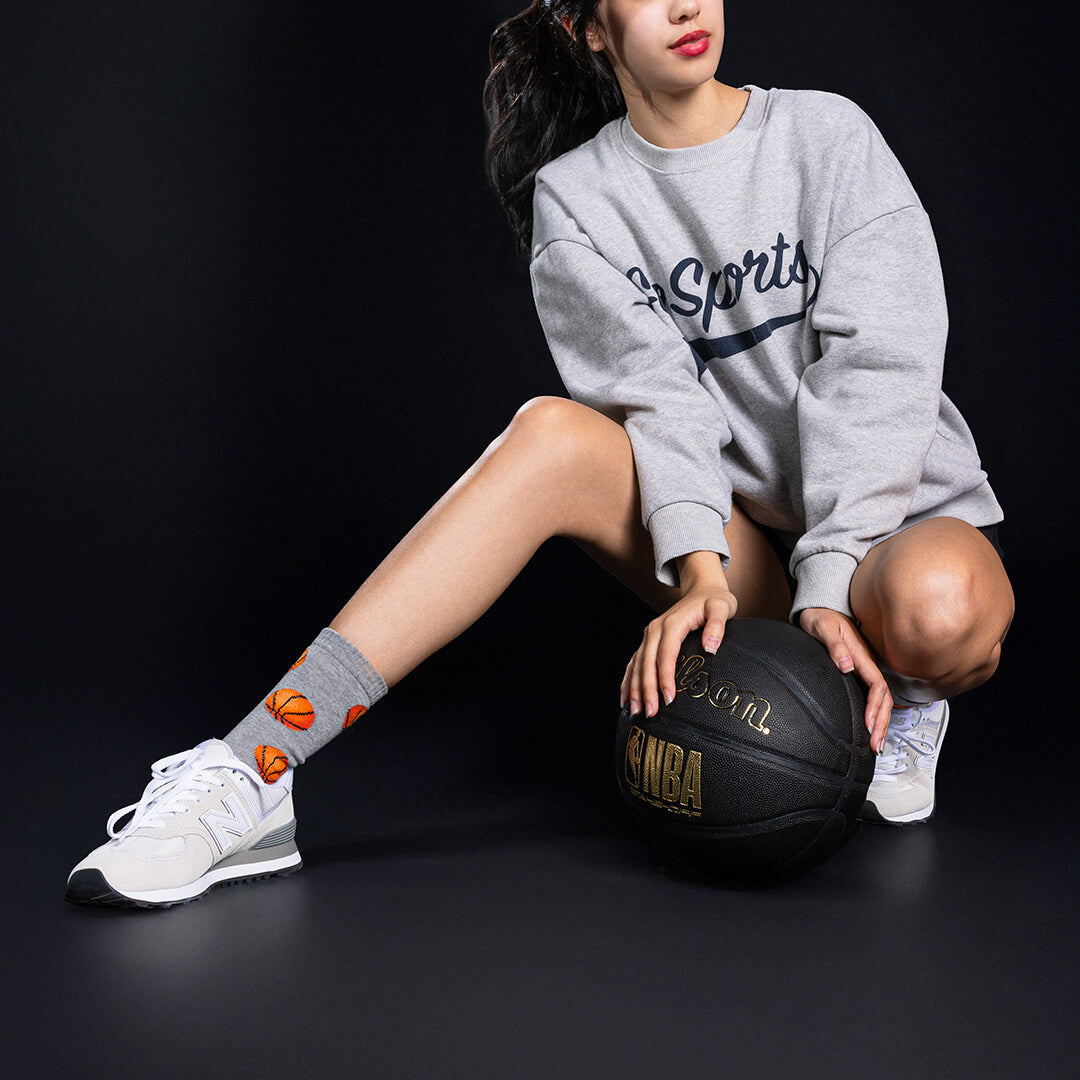 Person wearing a gray sweatshirt and white sneakers with a basketball on a black background