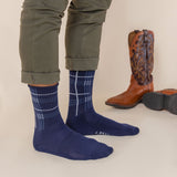 Person wearing blue plaid socks with brown cowboy boots on a neutral background thumbnail