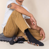 Person wearing black socks with patterned toes and heels, sitting on a beige surface.
