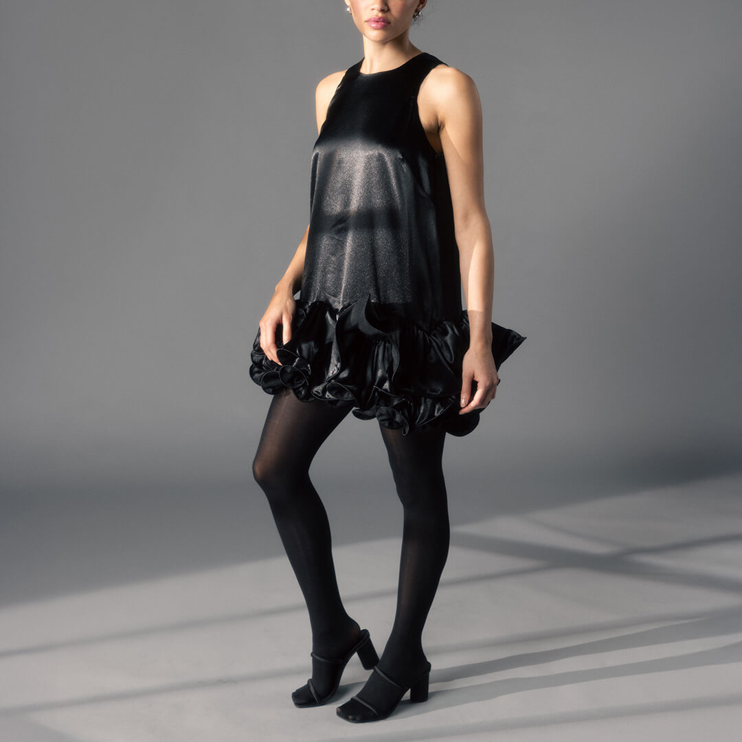 Woman wearing a black dress with ruffled layers and tights on a gray background