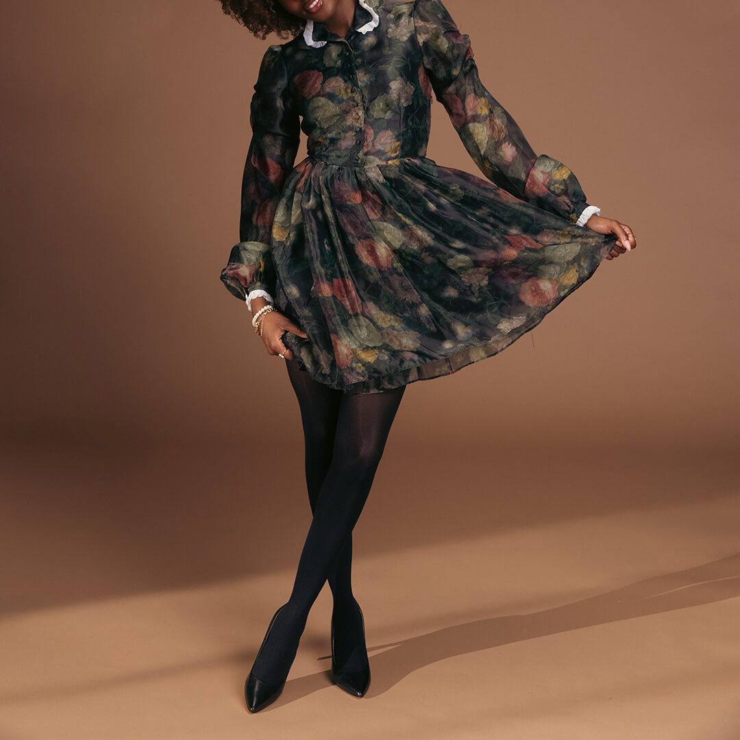 Woman wearing a floral dress with black tights and heels on a brown background