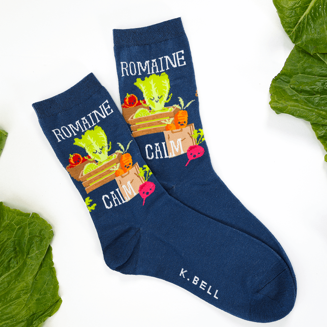 Navy blue socks with vegetable design and 'K. Bell' branding on a white background with green leaves.