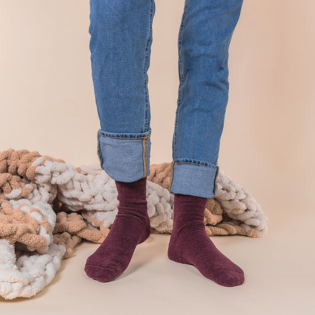 Person wearing maroon velvet socks with rolled-up blue jeans against a beige background