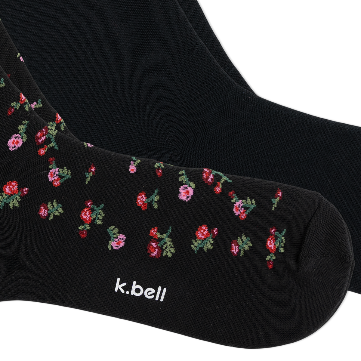 Black crew socks with a small pink and red floral pattern and green leaves, featuring the white text 'k.bell' near the toe, shown on a white background.