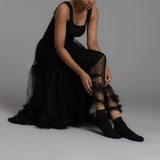 Person wearing a black dress and black  laced ankle socks on a gray background