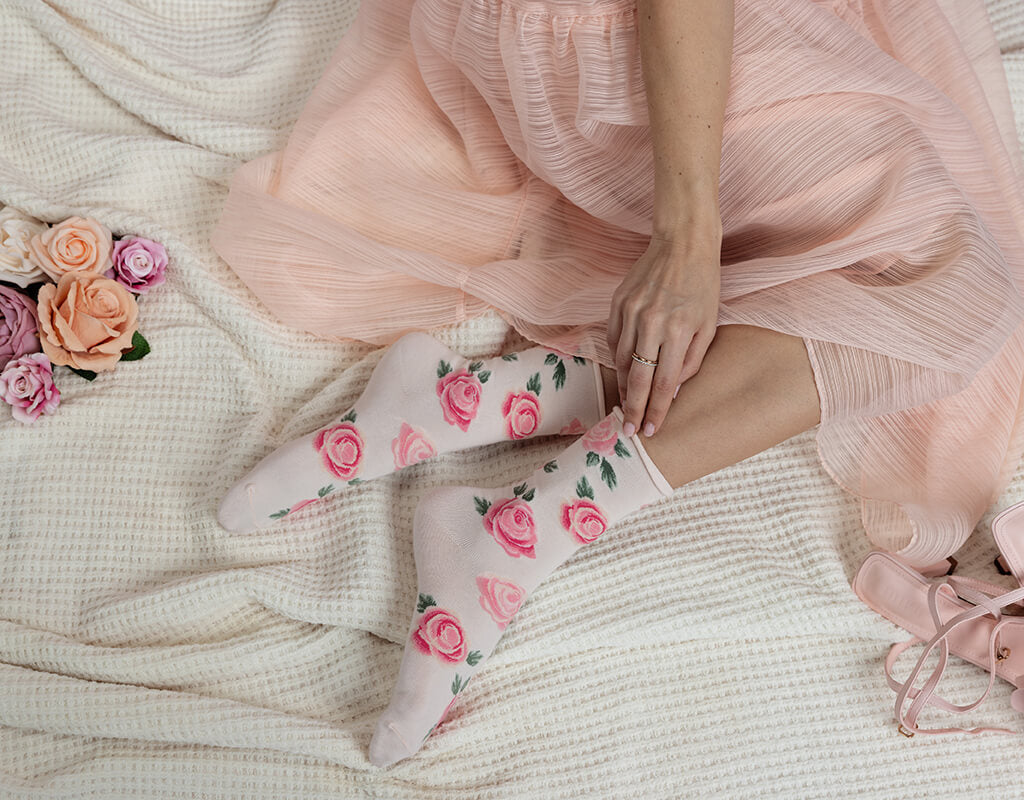 Person wearing pink floral socks with a light pink dress on a textured surface.
