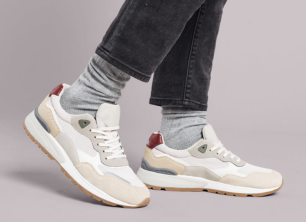 White sneakers with brown accents and gray K.Bell crew socks worn by a person on a gray background