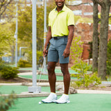 Man in yellow shirt and gray shorts holding a golf club on a putting green. thumbnail