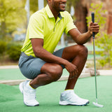 Man in a yellow shirt and gray shorts crouching on a golf course holding a golf club.