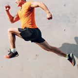 Man in orange shirt and black shorts running in front of a concrete surface