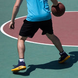Person holding a basketball on a court wearing a blue shirt, black shorts, and colorful shoes.