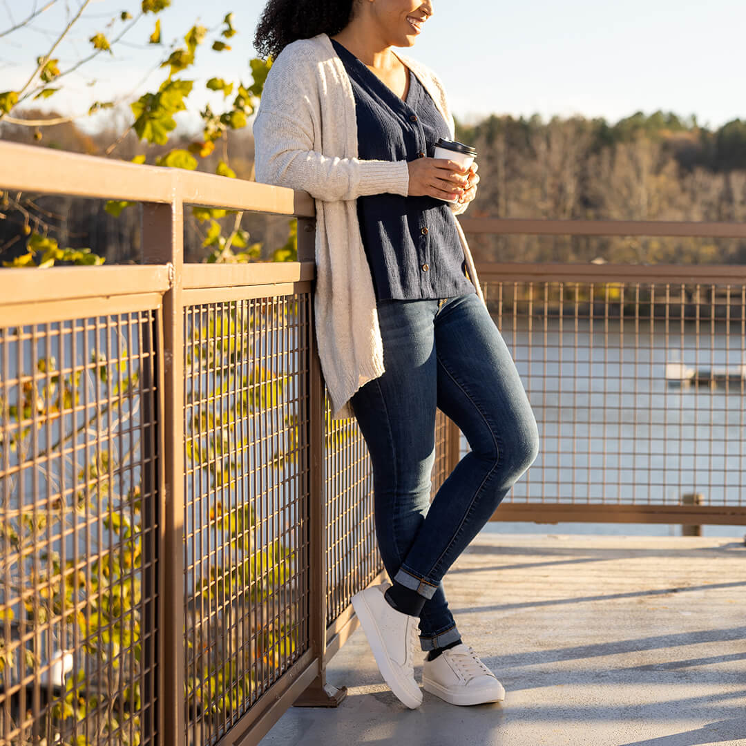 Woman standing on a bridge holding a coffee cup with a scenic background