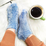 Person wearing fuzzy. blue ankle socks and tan sweats, sitting next to a cup of coffee. thumbnail