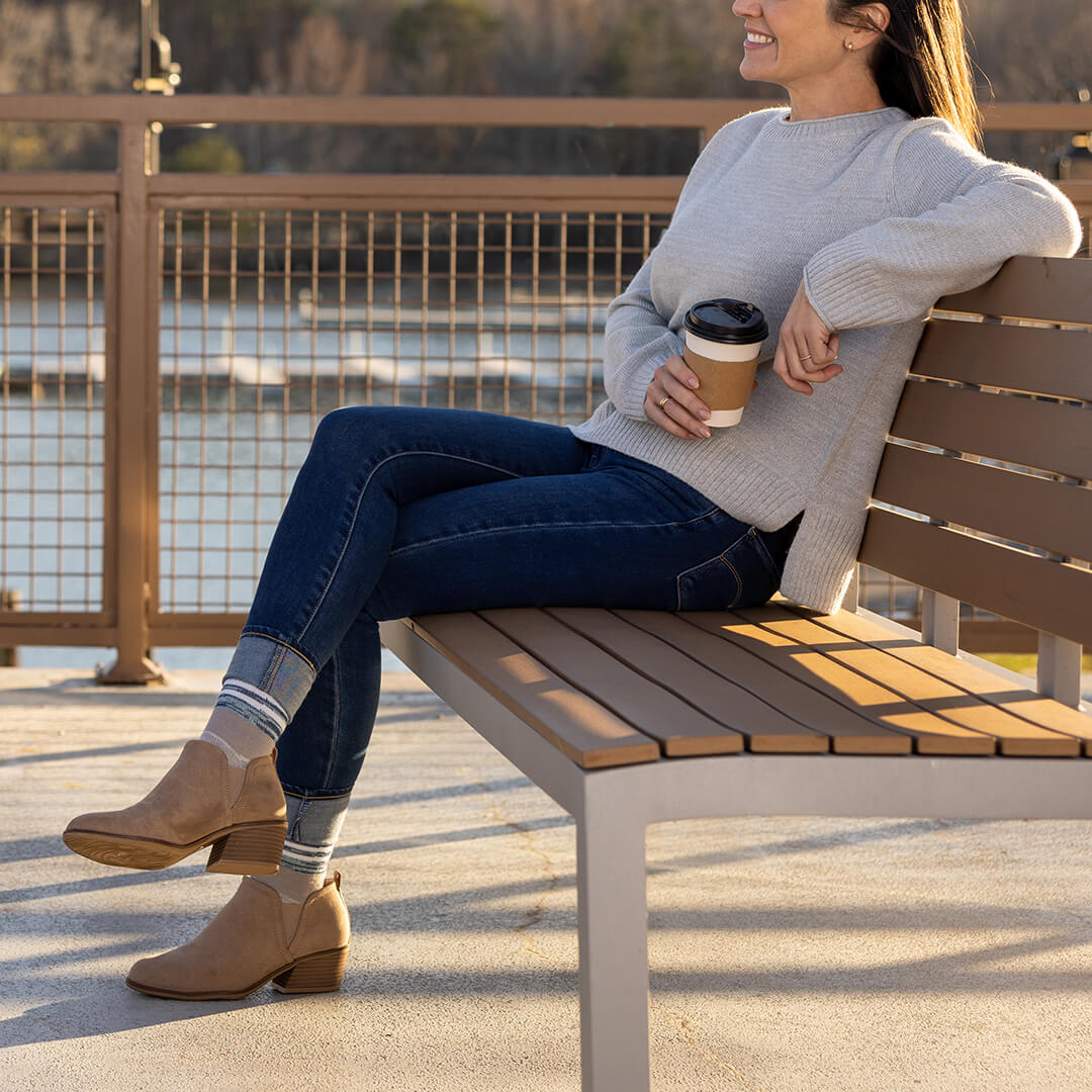 Woman sitting on a wooden bench by a waterfront, holding a coffee cup.